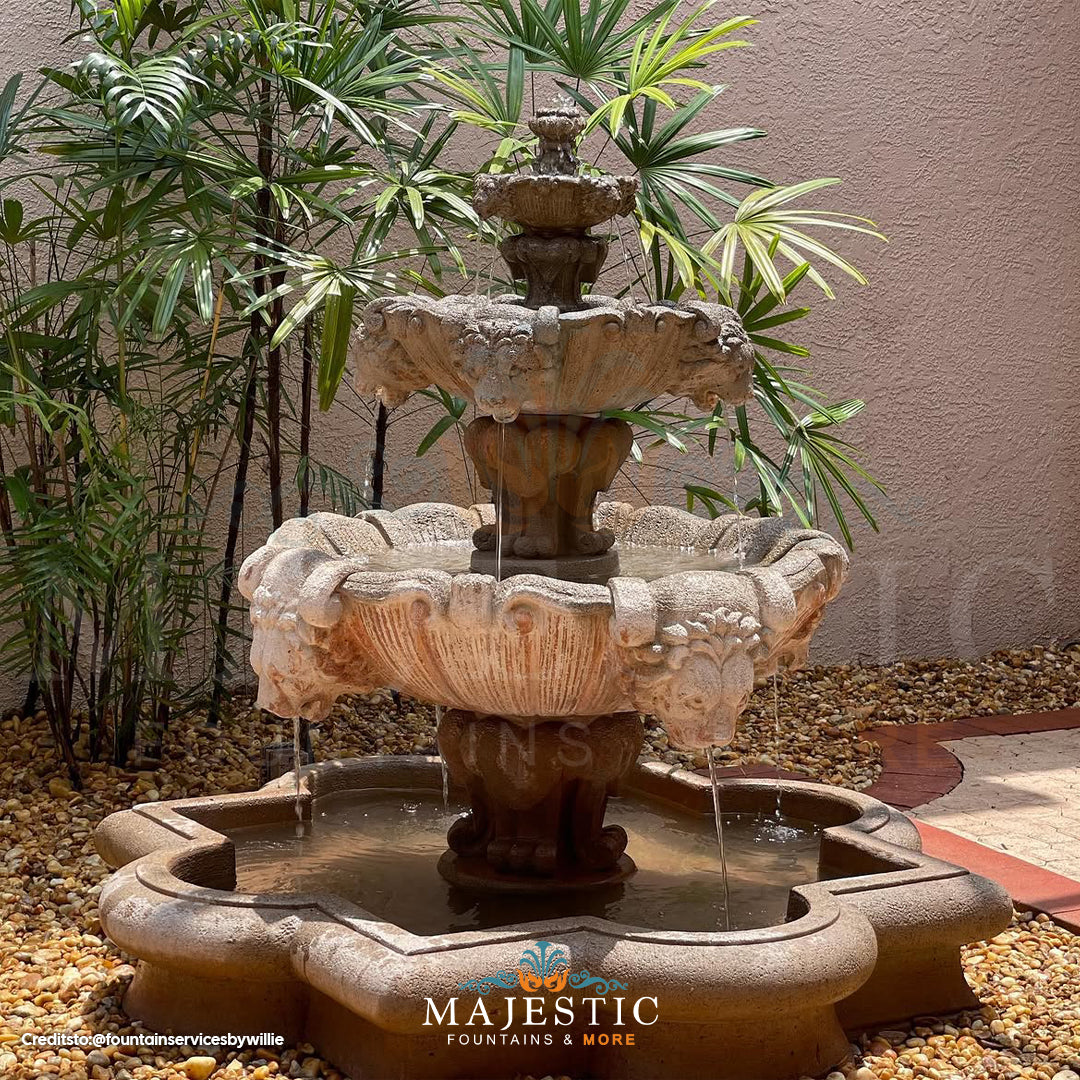 Fiore Stone 3 Tier Lion Fountain in cast stone flowing in a courtyard setting with a river rock base and green plants