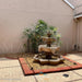Fiore Stone 3 Tier Lion Fountain in cast stone with basin set in a courtyard pebble bed bordered by brick and pavers