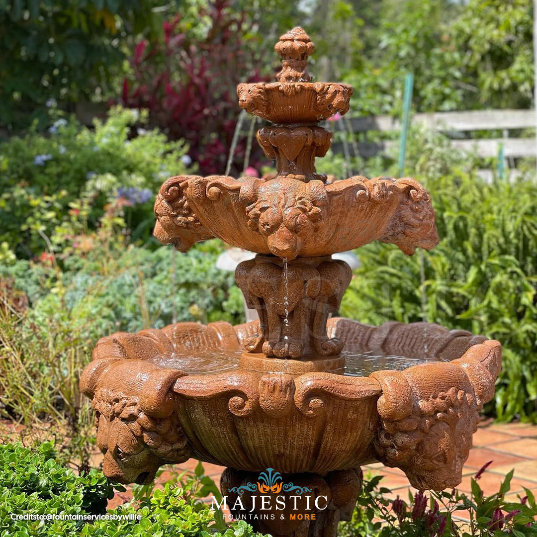 Fiore Stone 3 Tier Lion Fountain in cast stone with water flowing from lion heads on a brick patio in a lush garden