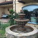 Fiore Stone Roma Fountain 234-F in cast stone on a patio with water flowing into a stone basin near a large window